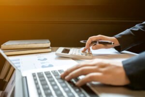 Imposto-de-Renda-2025.jpg" alt="Pessoa calculando valores com notebook e calculadora, simbolizando o preenchimento da declaração do Imposto de Renda 2025
