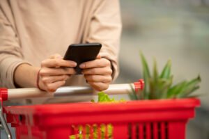 vale-alimentacao-planejamento-financeiro.jpg" alt="Pessoa com carrinho de supermercado usando celular, representando o uso do vale-alimentação e planejamento financeiro nas compras