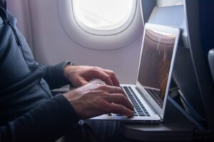 Profissional usando notebook durante voo, representando como economizar com viagens corporativas mantendo a produtividade"