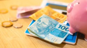 Notas e moedas de real brasileiro ao lado de um cofrinho rosa e uma calculadora, simbolizando planejamento financeiro e investimentos em renda fixa
