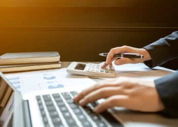 Imposto-de-Renda-2025.jpg" alt="Pessoa calculando valores com notebook e calculadora, simbolizando o preenchimento da declaração do Imposto de Renda 2025