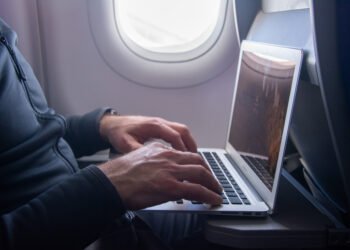 Profissional usando notebook durante voo, representando como economizar com viagens corporativas mantendo a produtividade"