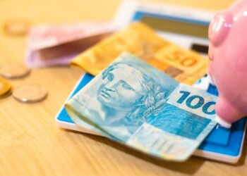 Notas e moedas de real brasileiro ao lado de um cofrinho rosa e uma calculadora, simbolizando planejamento financeiro e investimentos em renda fixa